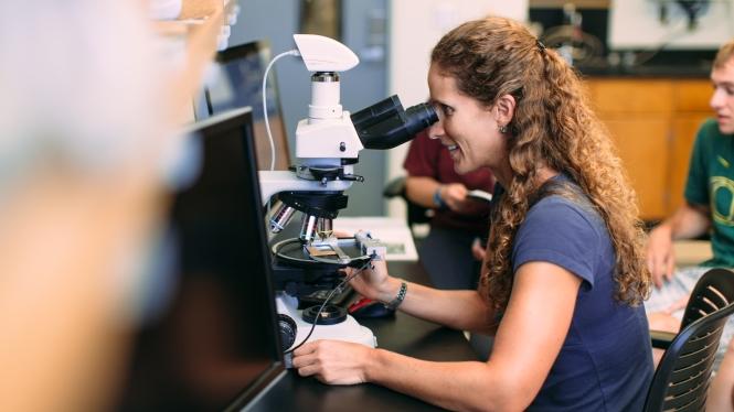 Picture of Kathy Surpless looking through a microscope in a science lab. 