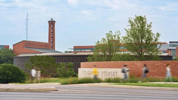 Students walk on the sidewalk beside the Trinity University entrance sign