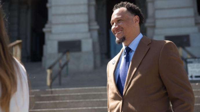 Terris Tiller stands outside smiling in a brown suit