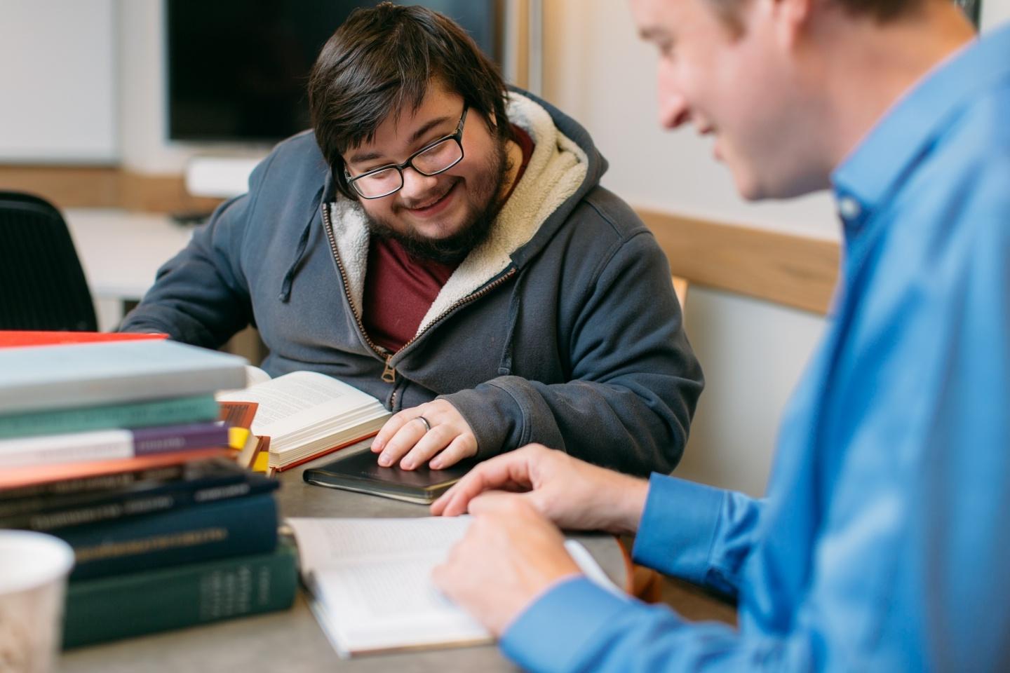 Two students engaged in conversation with a stack of books on their table